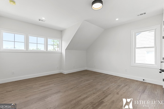 additional living space with vaulted ceiling, wood finished floors, visible vents, and baseboards