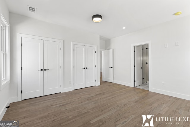 unfurnished bedroom featuring wood finished floors, two closets, visible vents, and baseboards