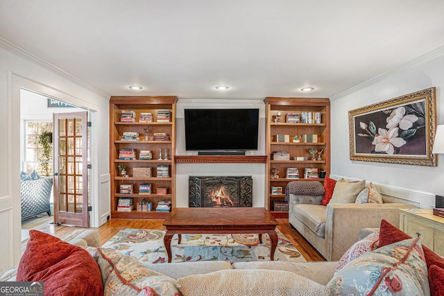 living room featuring built in shelves, a lit fireplace, ornamental molding, recessed lighting, and wood finished floors