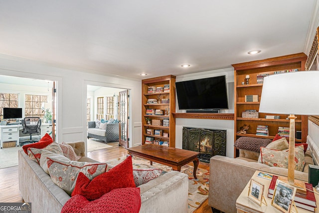 living area with light wood-type flooring, a warm lit fireplace, and crown molding