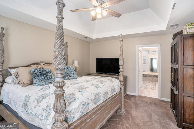 carpeted bedroom featuring a tray ceiling, baseboards, visible vents, and connected bathroom