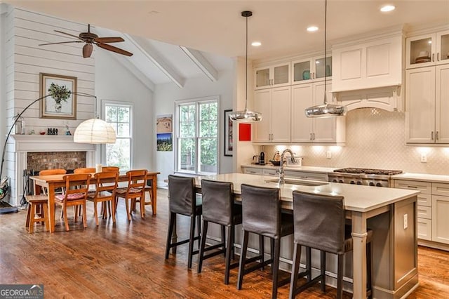 kitchen with a fireplace, light countertops, lofted ceiling with beams, a sink, and an island with sink