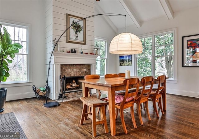 dining area with vaulted ceiling with beams, a fireplace, wood finished floors, and baseboards