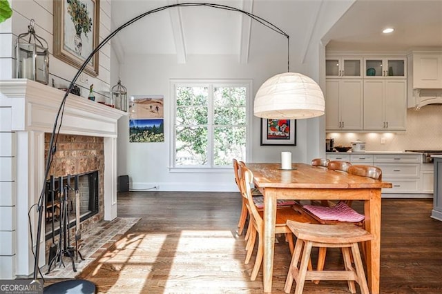 dining room with beam ceiling, baseboards, dark wood finished floors, and a tiled fireplace