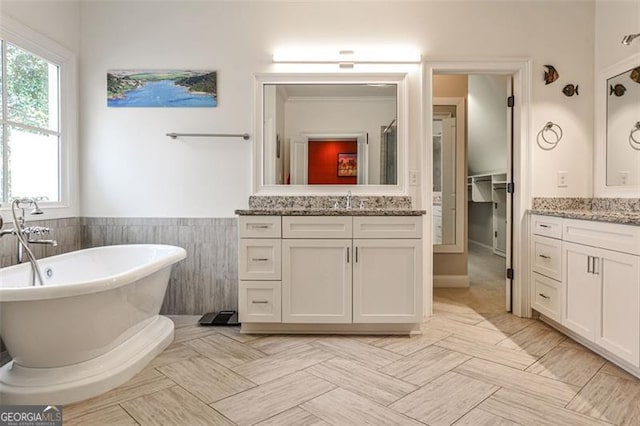 bathroom featuring tile walls, a wainscoted wall, two vanities, a freestanding tub, and a sink