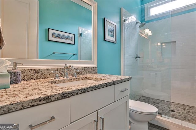 bathroom featuring a tile shower, vanity, and toilet