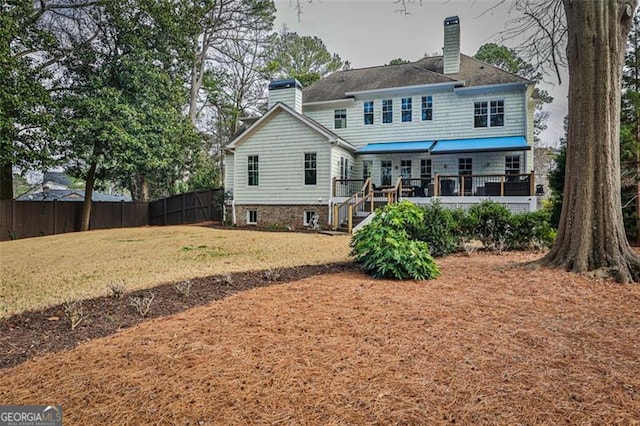 back of house with a deck, a chimney, fence, and a lawn