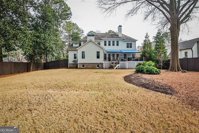 rear view of property featuring a chimney, a fenced backyard, and a lawn