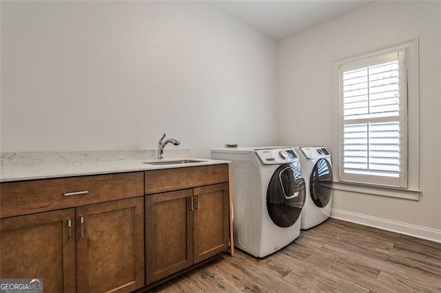 laundry area featuring cabinet space, baseboards, light wood-style flooring, washing machine and clothes dryer, and a sink