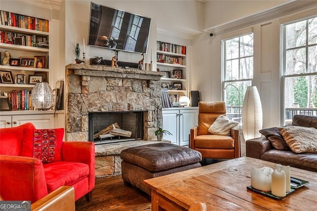 living area featuring built in shelves, a wealth of natural light, a fireplace, and wood finished floors