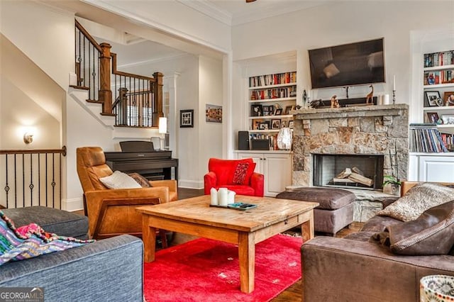 sitting room with a stone fireplace, built in shelves, baseboards, ornamental molding, and stairway