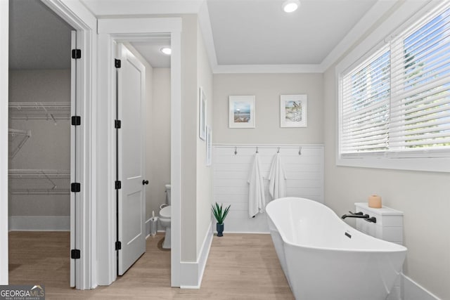 bathroom with toilet, wood finished floors, a freestanding bath, a walk in closet, and crown molding