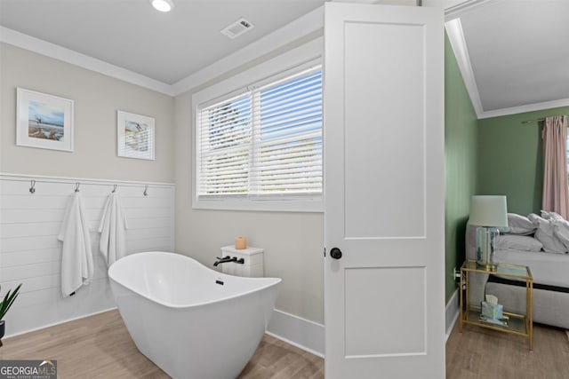 bathroom featuring a freestanding bath, ornamental molding, wood finished floors, and visible vents