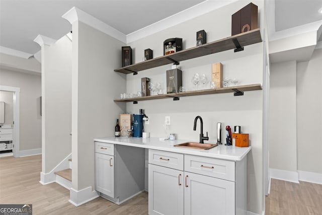 bar featuring a sink, baseboards, stairs, light wood finished floors, and indoor wet bar