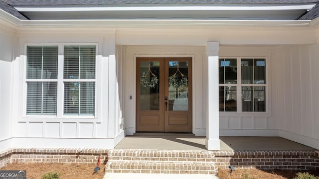 view of exterior entry with board and batten siding, french doors, and roof with shingles