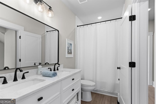 full bathroom featuring double vanity, a sink, toilet, and wood finished floors