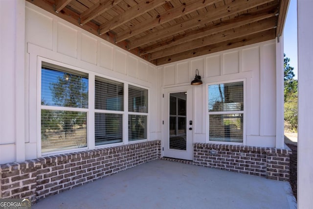 view of exterior entry featuring a patio, board and batten siding, and brick siding