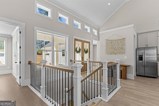 hallway featuring light wood-style floors, baseboards, crown molding, and an upstairs landing