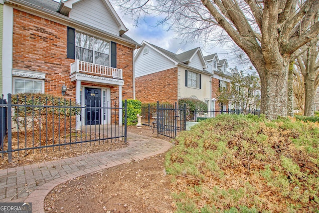 view of side of home featuring brick siding, a fenced front yard, and a balcony