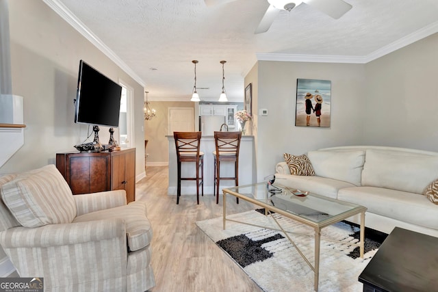 living room featuring a textured ceiling, light wood-style flooring, ceiling fan with notable chandelier, baseboards, and ornamental molding