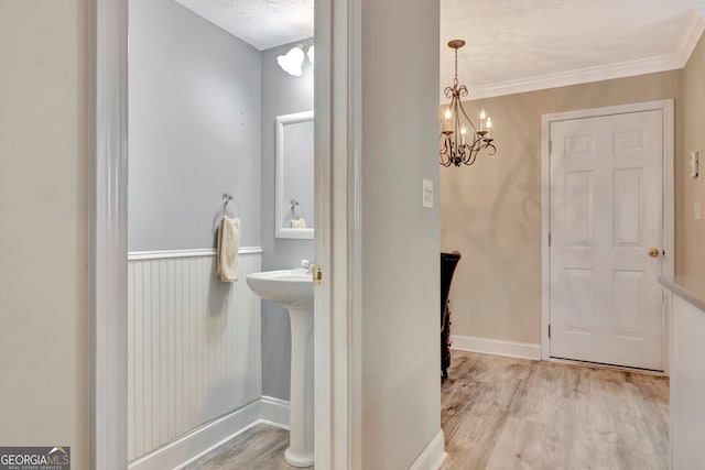 bathroom featuring crown molding, a textured ceiling, wood finished floors, a chandelier, and baseboards