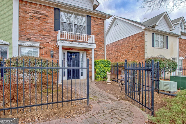 exterior space featuring a fenced front yard, brick siding, a gate, central AC, and a balcony