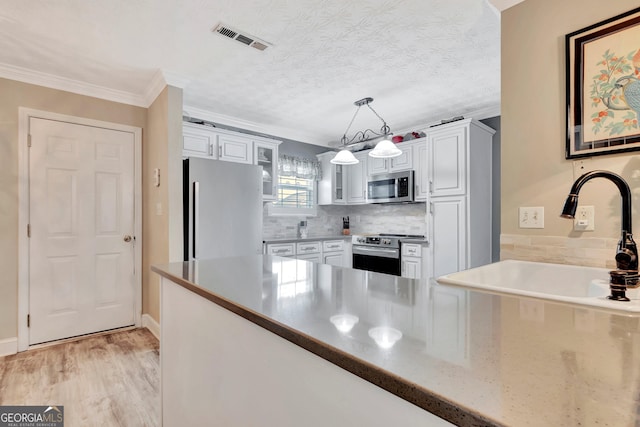 kitchen featuring visible vents, glass insert cabinets, appliances with stainless steel finishes, a sink, and backsplash