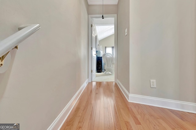 hall featuring lofted ceiling, light wood-style flooring, and baseboards