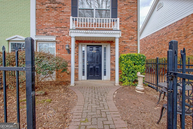 view of exterior entry featuring brick siding, fence, and a balcony