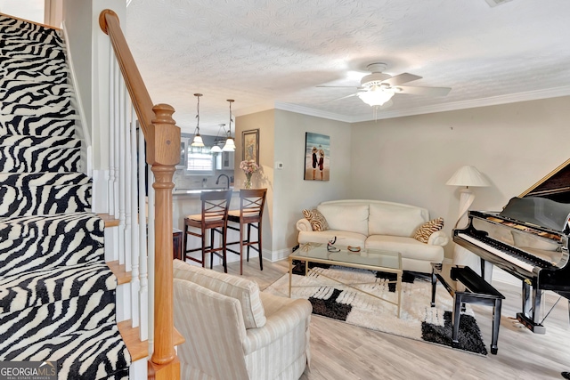 living room with baseboards, ceiling fan, wood finished floors, crown molding, and a textured ceiling