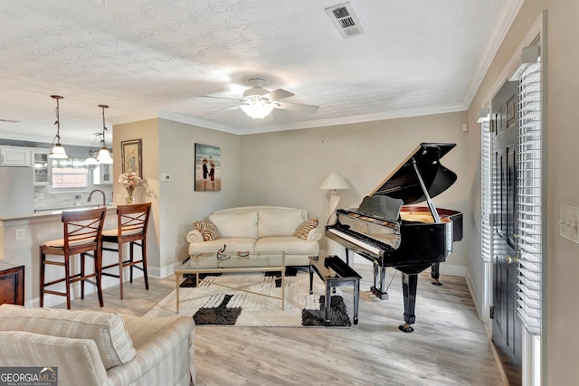 living room with visible vents, a ceiling fan, a textured ceiling, crown molding, and light wood-type flooring