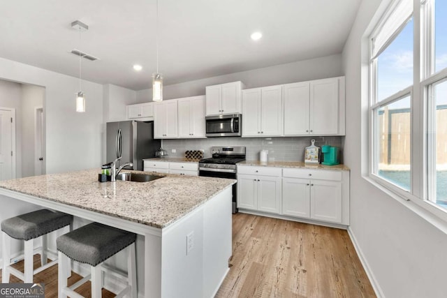 kitchen with light wood finished floors, stainless steel appliances, backsplash, white cabinets, and a sink