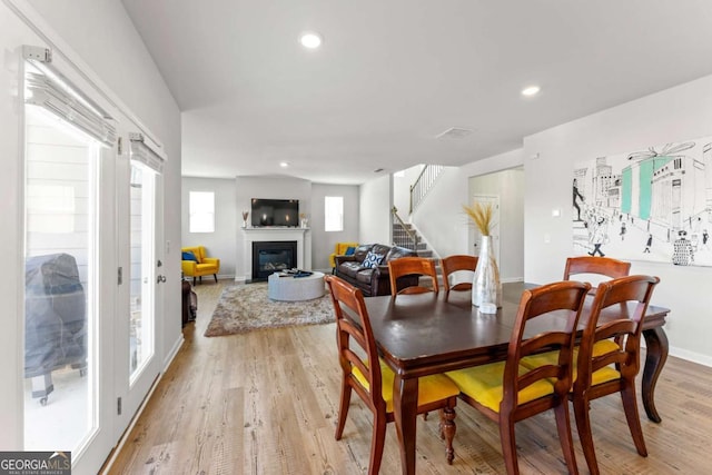 dining room with baseboards, a glass covered fireplace, light wood-style flooring, stairs, and recessed lighting