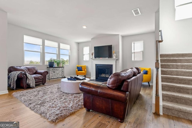 living room featuring visible vents, a glass covered fireplace, wood finished floors, baseboards, and stairs