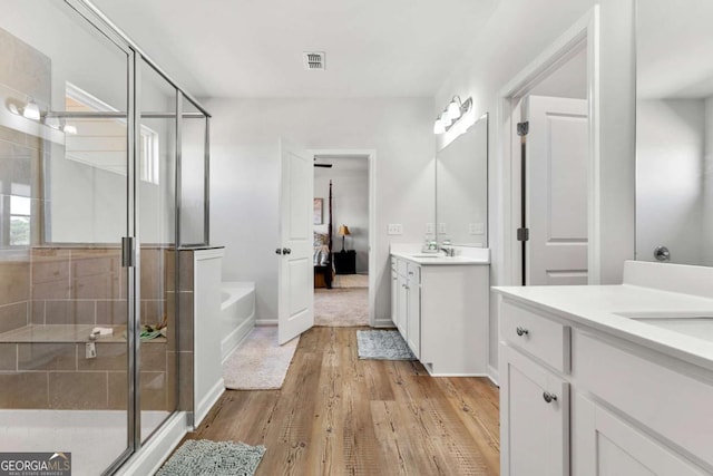 ensuite bathroom with a garden tub, wood finished floors, two vanities, visible vents, and a stall shower