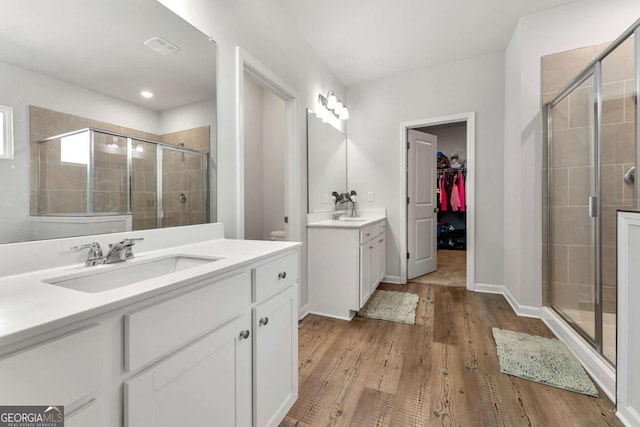 full bathroom featuring a stall shower, wood finished floors, a sink, a spacious closet, and two vanities