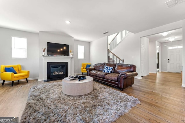 living area featuring baseboards, visible vents, a glass covered fireplace, wood finished floors, and stairs