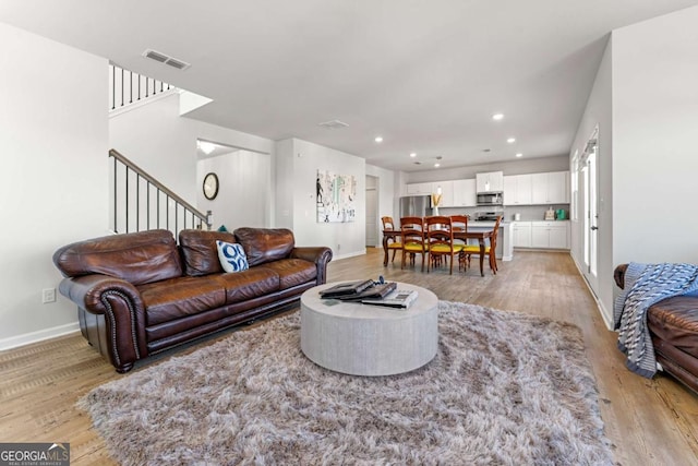 living area with stairs, visible vents, and light wood-style floors