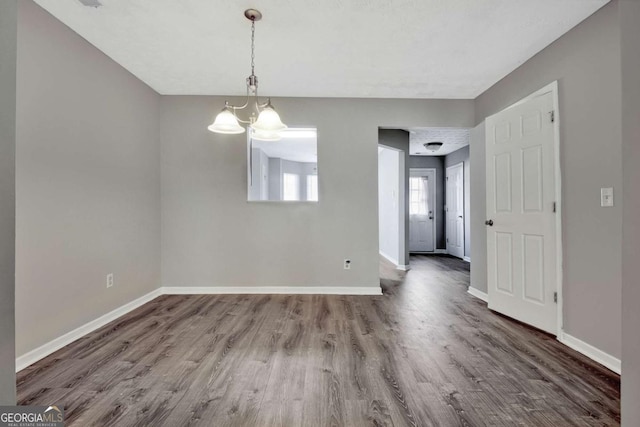 unfurnished dining area featuring a chandelier, wood finished floors, and baseboards