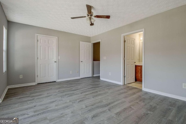 unfurnished bedroom with a textured ceiling, ensuite bathroom, wood finished floors, and baseboards