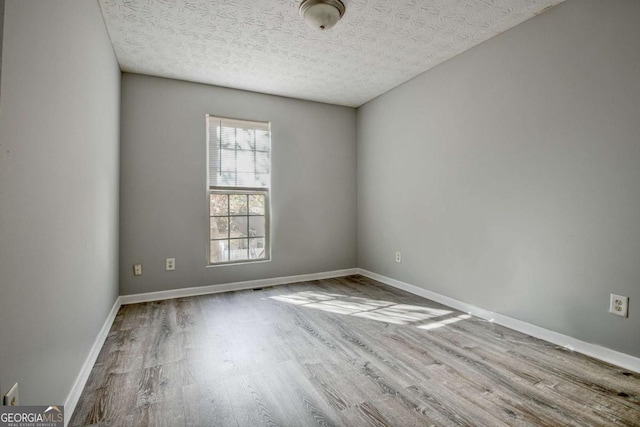 unfurnished room with visible vents, a textured ceiling, baseboards, and wood finished floors