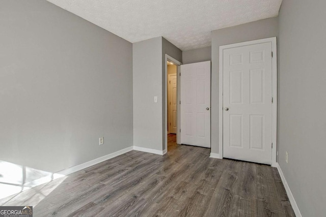 unfurnished bedroom with a textured ceiling, baseboards, and wood finished floors