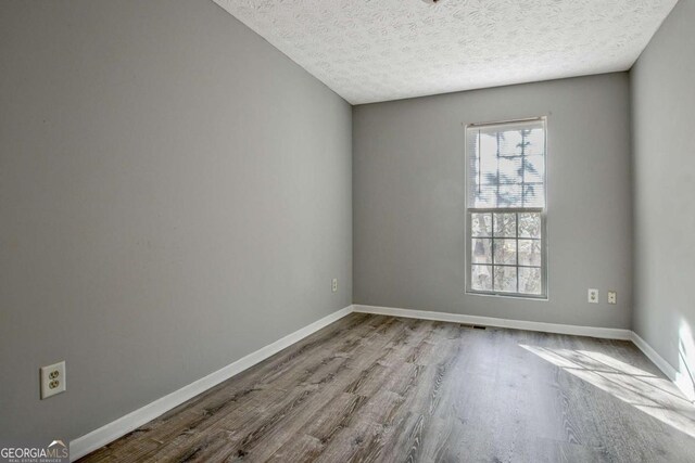 spare room with a textured ceiling, baseboards, and wood finished floors