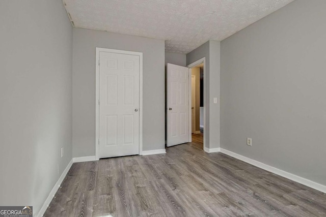 unfurnished bedroom with a textured ceiling, wood finished floors, and baseboards