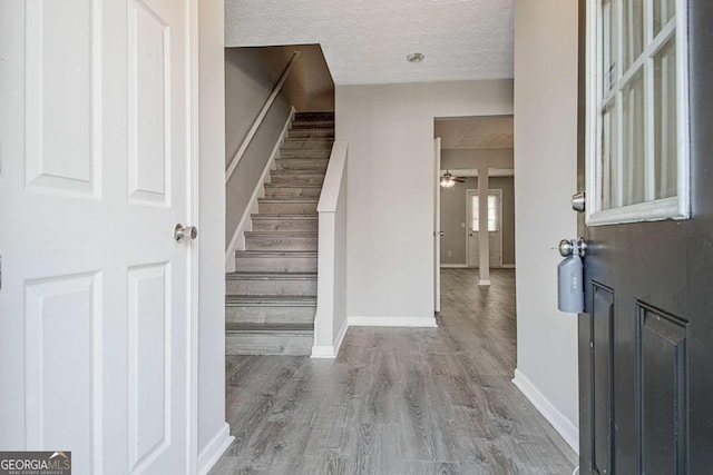 foyer featuring baseboards, a textured ceiling, stairway, and wood finished floors