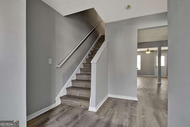 stairs featuring ceiling fan, a textured ceiling, baseboards, and wood finished floors