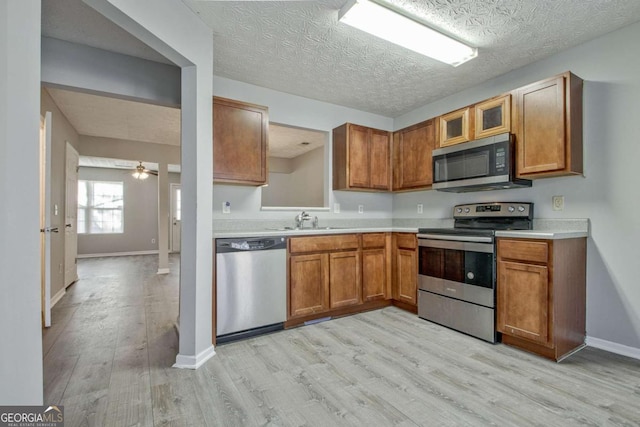 kitchen with brown cabinets, light countertops, appliances with stainless steel finishes, a sink, and light wood-type flooring