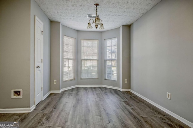 unfurnished dining area featuring a chandelier, a textured ceiling, dark wood-style flooring, visible vents, and baseboards