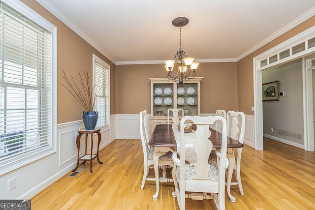 dining area with crown molding, visible vents, light wood-style floors, wainscoting, and a chandelier