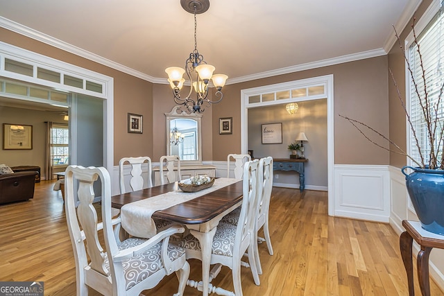 dining area featuring light wood finished floors, a wainscoted wall, an inviting chandelier, crown molding, and a decorative wall